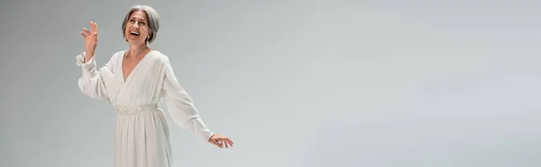 Amazed middle aged bride in white wedding dress gesturing isolated on grey, banner — Stockfoto