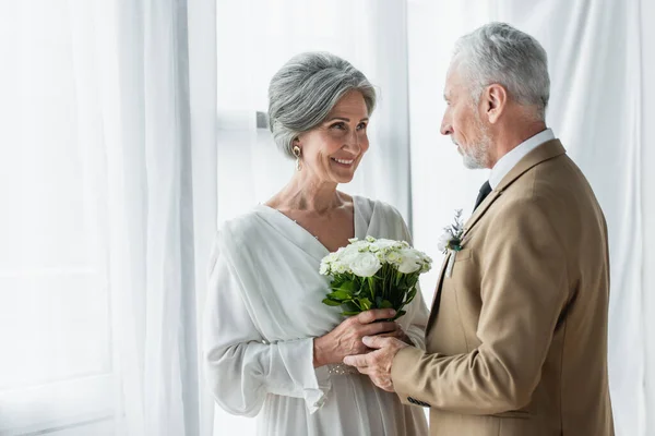 Bearded middle aged groom giving wedding bouquet to happy bride in white dress — Foto stock