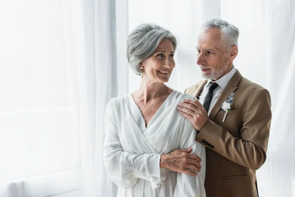 Bearded middle aged groom in suit touching shoulder of cheerful bride in white dress — Photo de stock