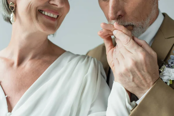 Cropped view of bearded middle aged man kissing hand of happy bride in white wedding dress isolated on grey — Photo de stock
