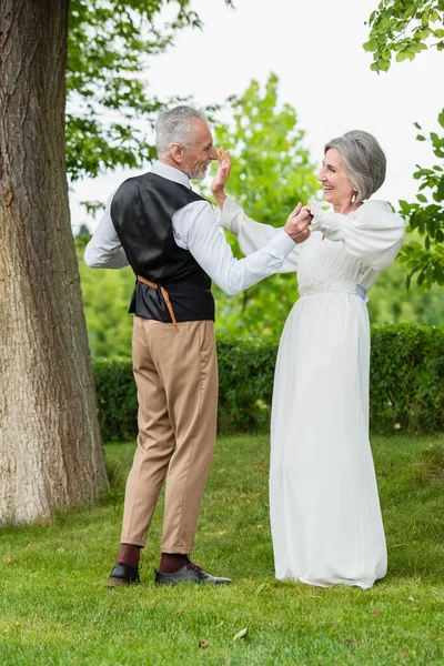 Happy mature man in formal wear dancing with bride in white wedding dress in green garden — Fotografia de Stock