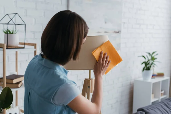 Back view of brunette woman wiping lamp with soft rag at home — Stock Photo