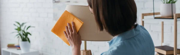 Brunette woman wiping lamp with rag at home, banner — Stock Photo