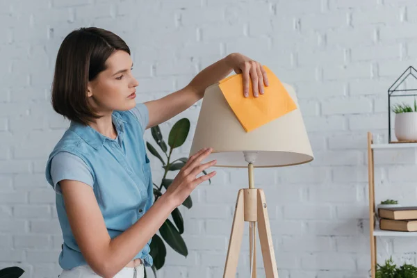 Молода брюнетка жінка прибирає лампу з ганчіркою у вітальні — стокове фото