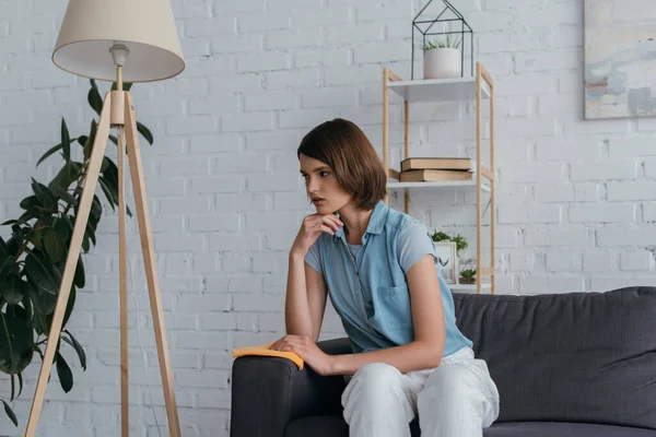 Tired woman with rag sitting on couch in living room near floor lamp — Foto stock