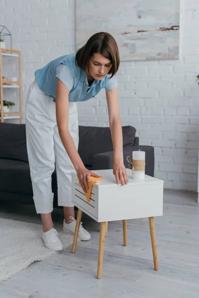 Полная длина молодая брюнетка женщина уборка прикроватный столик на дому — стоковое фото