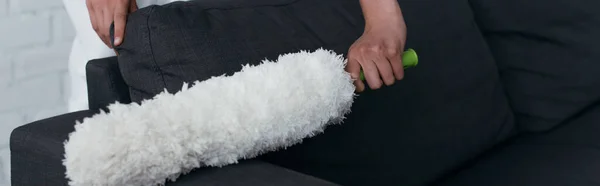 Обрезанный вид на диван уборщицы домохозяйки с пыльной щеткой, баннер — стоковое фото