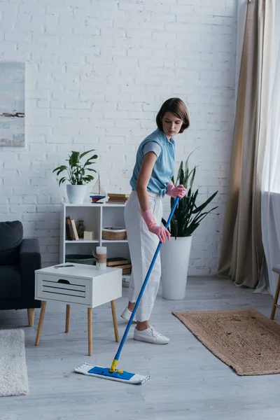 Full length of brunette woman cleaning floor in living room at home — Stock Photo