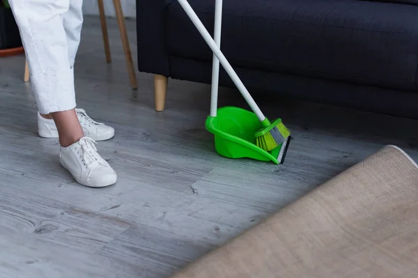 Cropped view of woman in white sneakers near broom and scoop at home — Stock Photo