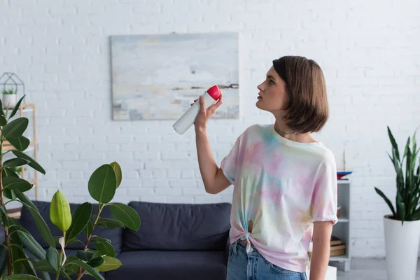 Side view of woman spraying air freshener in living room - foto de stock