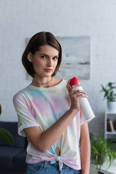 Young woman looking at camera and holding air freshener at home — Stock Photo