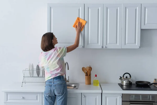 Вид сбоку на молодую женщину, чистившую белый шкаф на кухне — стоковое фото