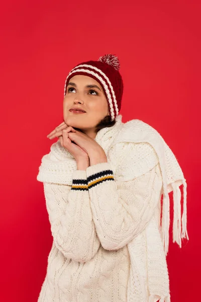 Dreamy woman in hat and knitted scarf looking away isolated on red — Photo de stock