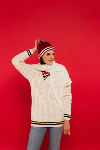 Smiling woman in hat and knitted clothes looking away isolated on red — Fotografia de Stock