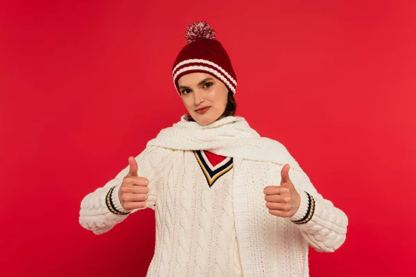 Smiling woman in warm clothes showing thumbs up isolated on red — Stock Photo