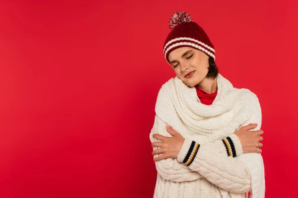 Pleased woman in knitted clothes closing eyes isolated on red — Stockfoto
