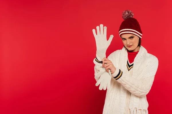 Smiling woman in knitted clothes wearing glove isolated on red — Stockfoto