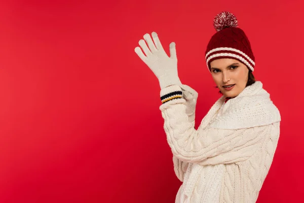 Smiling woman in warm clothes and hat wearing gloves isolated on red — Photo de stock