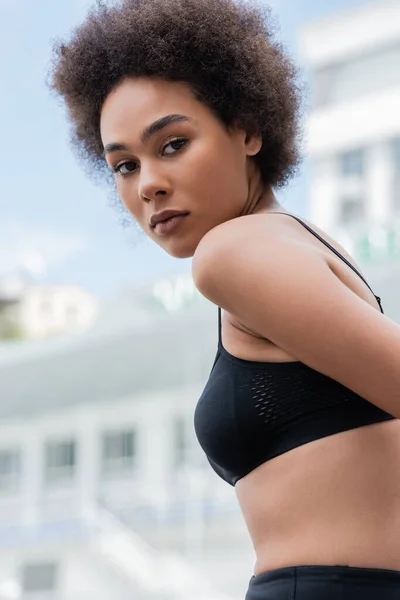 Athletic african american woman in black sports bra looking at camera outdoors — Photo de stock