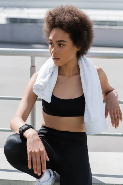 African american woman in black sports bra and with white towel looking away outdoors — Photo de stock