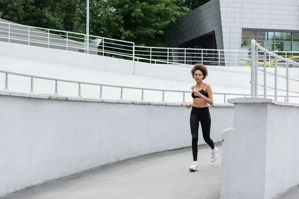 Full length of slim african american woman in black sportswear running outdoors — Photo de stock