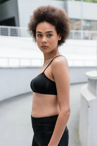 Slim african american woman in black sports bra looking at camera outdoors — Fotografia de Stock