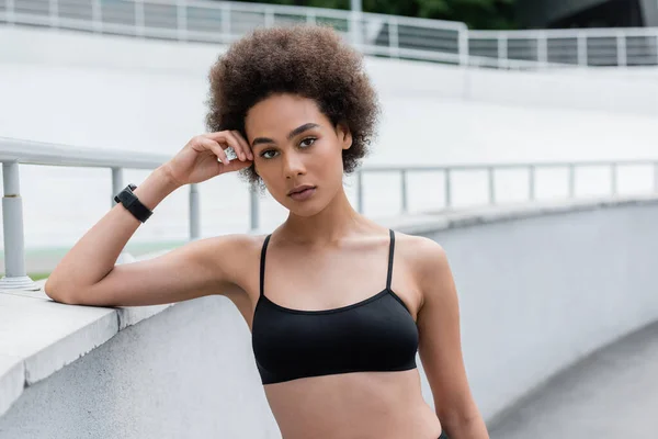 Athletic african american woman in black sports bra standing with hand near head — Stockfoto