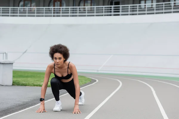 Young african american jogger standing in low start pose on track — Stock Photo
