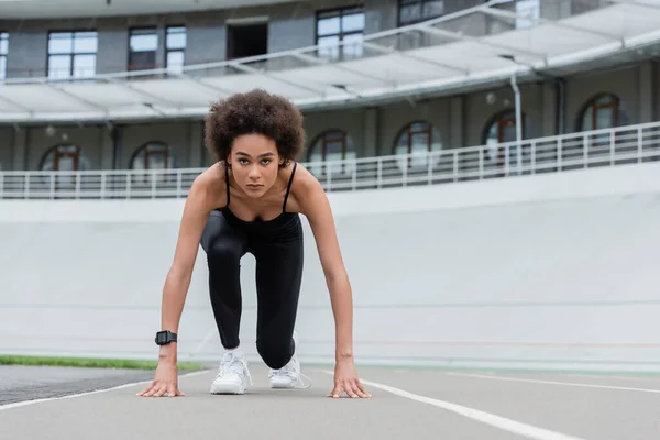 Front view of african american woman in sportswear and fitness tracker standing in low start pose - foto de stock