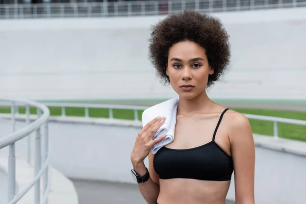 Young african american woman in fitness tracker standing with white towel on shoulder — Fotografia de Stock