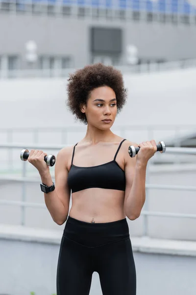 Athletic african american woman in black sports bra training with dumbbells — Stock Photo