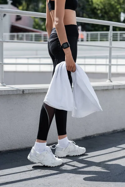 Cropped view of african american woman in black leggings and white sneakers holding white terry towel — Fotografia de Stock