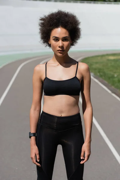 Front view of african american sportswoman in black sports bra and leggings looking at camera — Fotografia de Stock