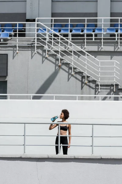 Thirsty african american sportswoman drinking water on urban stadium — Stock Photo