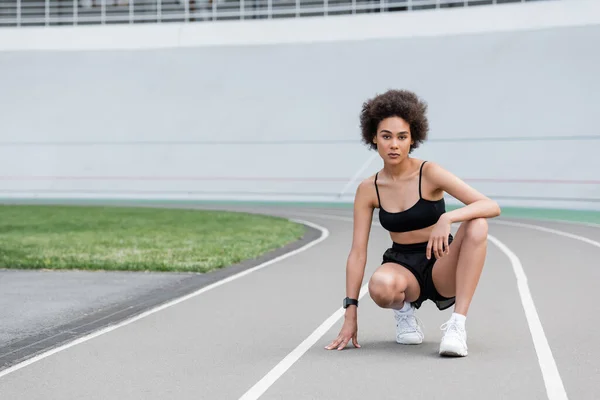 Slender african american sportswoman looking at camera while warming up on track — Fotografia de Stock