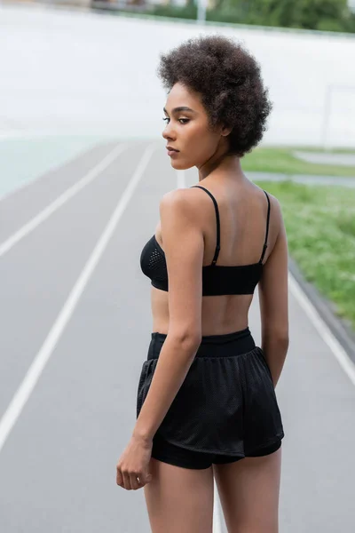 Young african american sportswoman in black sportswear standing on stadium — Stock Photo