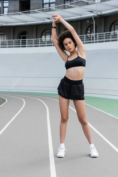 African american sportswoman in black sportswear stretching on stadium - foto de stock