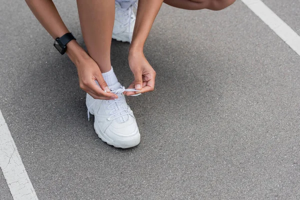 Cropped view of african american sportswoman tying shoelaces of sneaker on stadium — Stock Photo