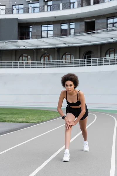 Африканская американская спортсменка в черной спортивной одежде стоит в позе на беговой дорожке — стоковое фото