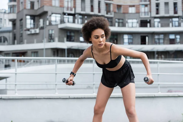 African american sportswoman exercising with dumbbells on blurred stadium — Stock Photo