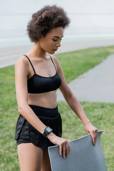 Young african american sportswoman holding fitness mat outdoors — Stock Photo