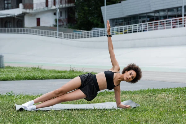 Fit african american sportswoman standing in side plank on fitness mat on stadium — Stockfoto