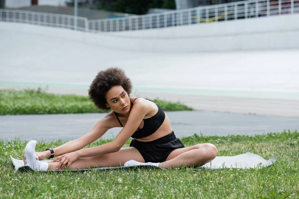 African american sportswoman stretching on fitness mat on stadium — Fotografia de Stock