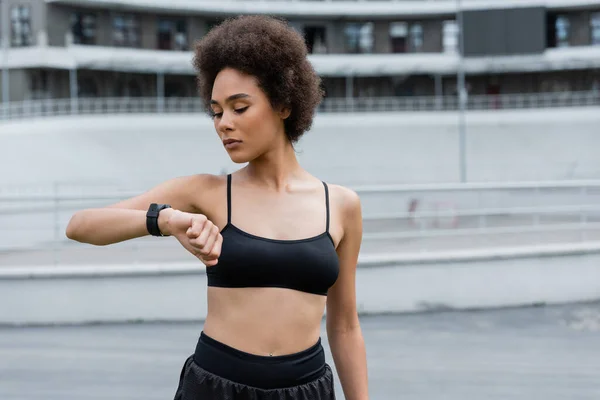 African american sportswoman looking at smart watch on blurred stadium - foto de stock