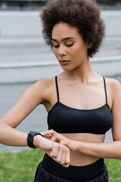 African american sportswoman in black top using fitness tracker on stadium - foto de stock