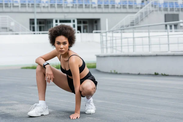 African american sportswoman in black sportswear and fitness tracker looking at camera on stadium — Stock Photo