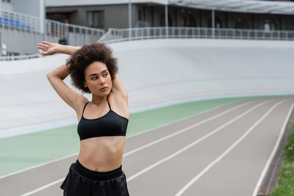 African american sportswoman stretching arms and looking away on stadium — Fotografia de Stock