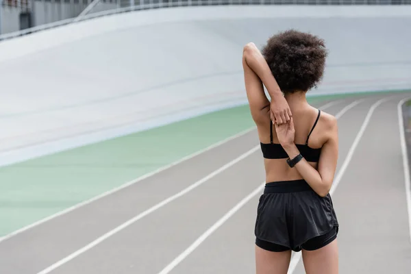 Back view of african american sportswoman stretching arms on blurred running track — Foto stock