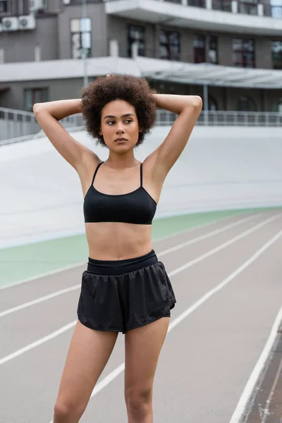 Fit african american woman in black sportswear standing on running track on stadium — Stock Photo