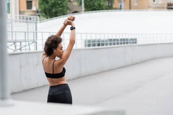 Side view of african american sportswoman in black top warming up on stadium at daytime — Stock Photo